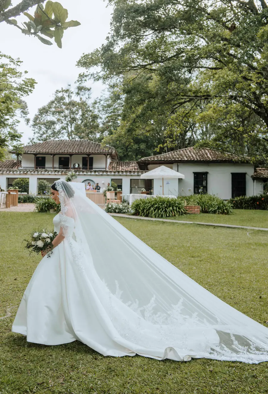 Novia caminando por un jardín con su vestido y velo extendidos